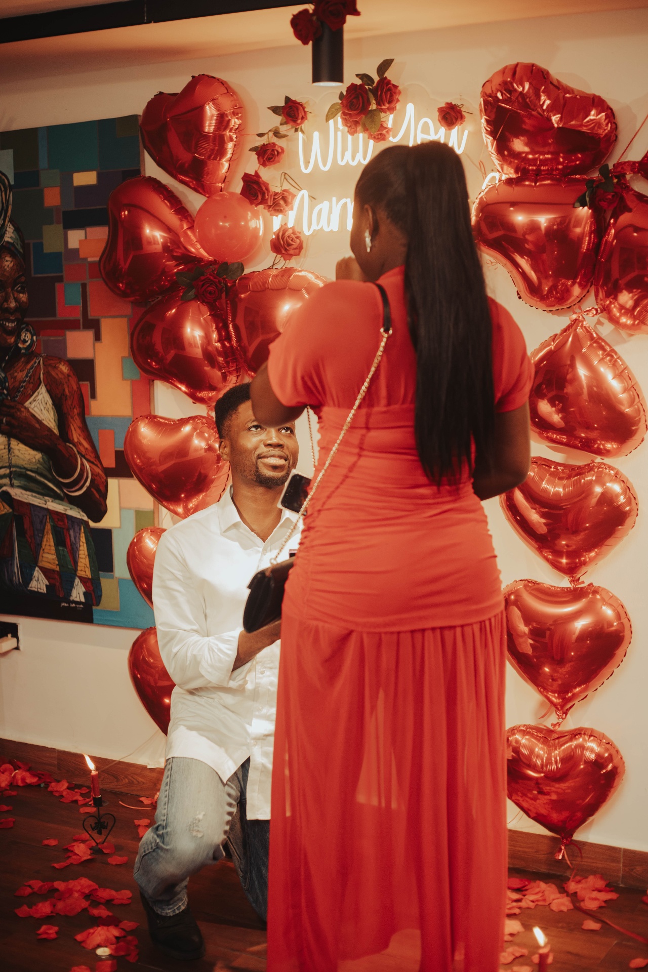 Kofo on one knee proposing, red 'Will You Marry Me' neon behind